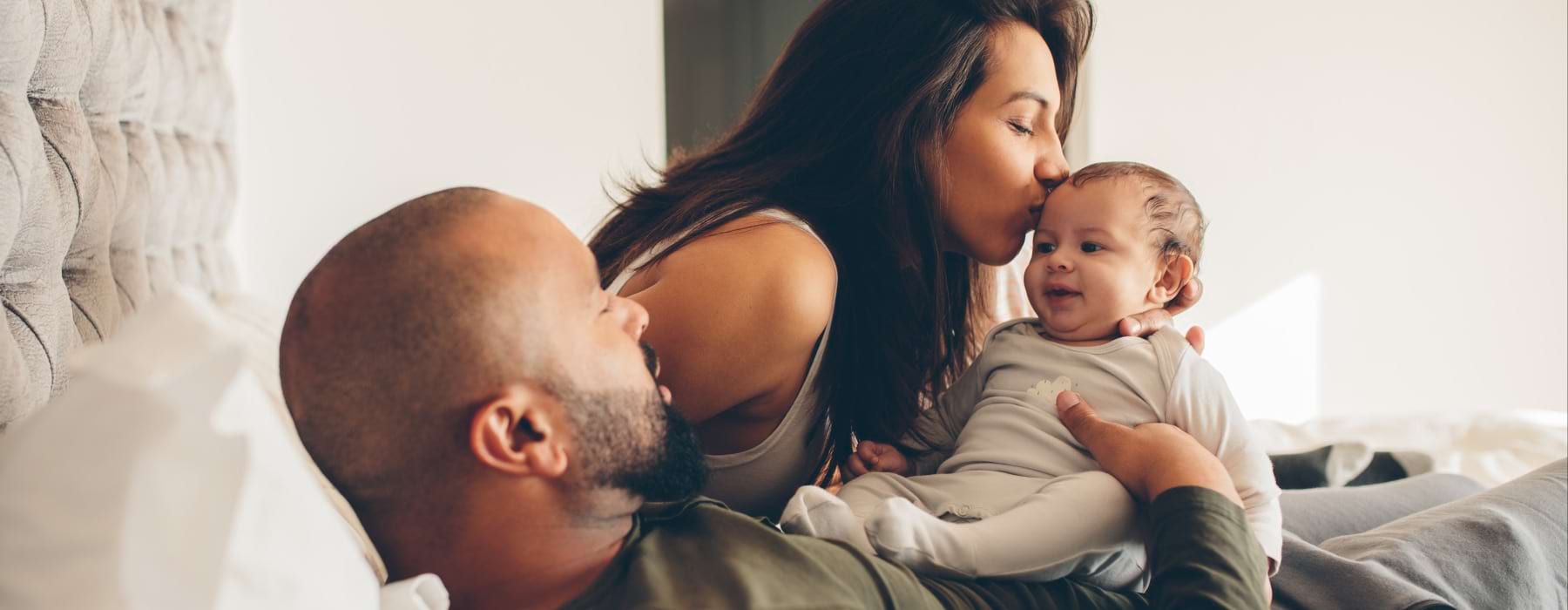 Couple laying in bed kissing their baby 